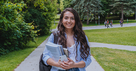 Student holding textbooks stands outside on campus